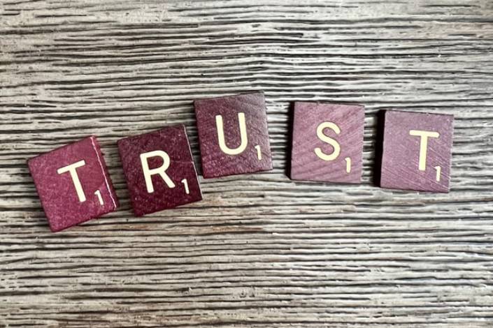 five burgundy scrabble tiles selling out TRUST on a wooden background 